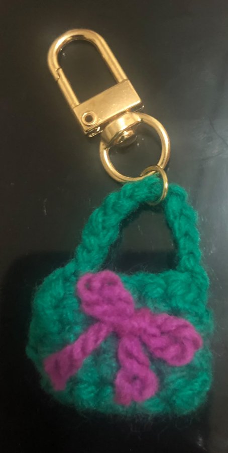 Handmade green crochet bag keychain with purple ribbon